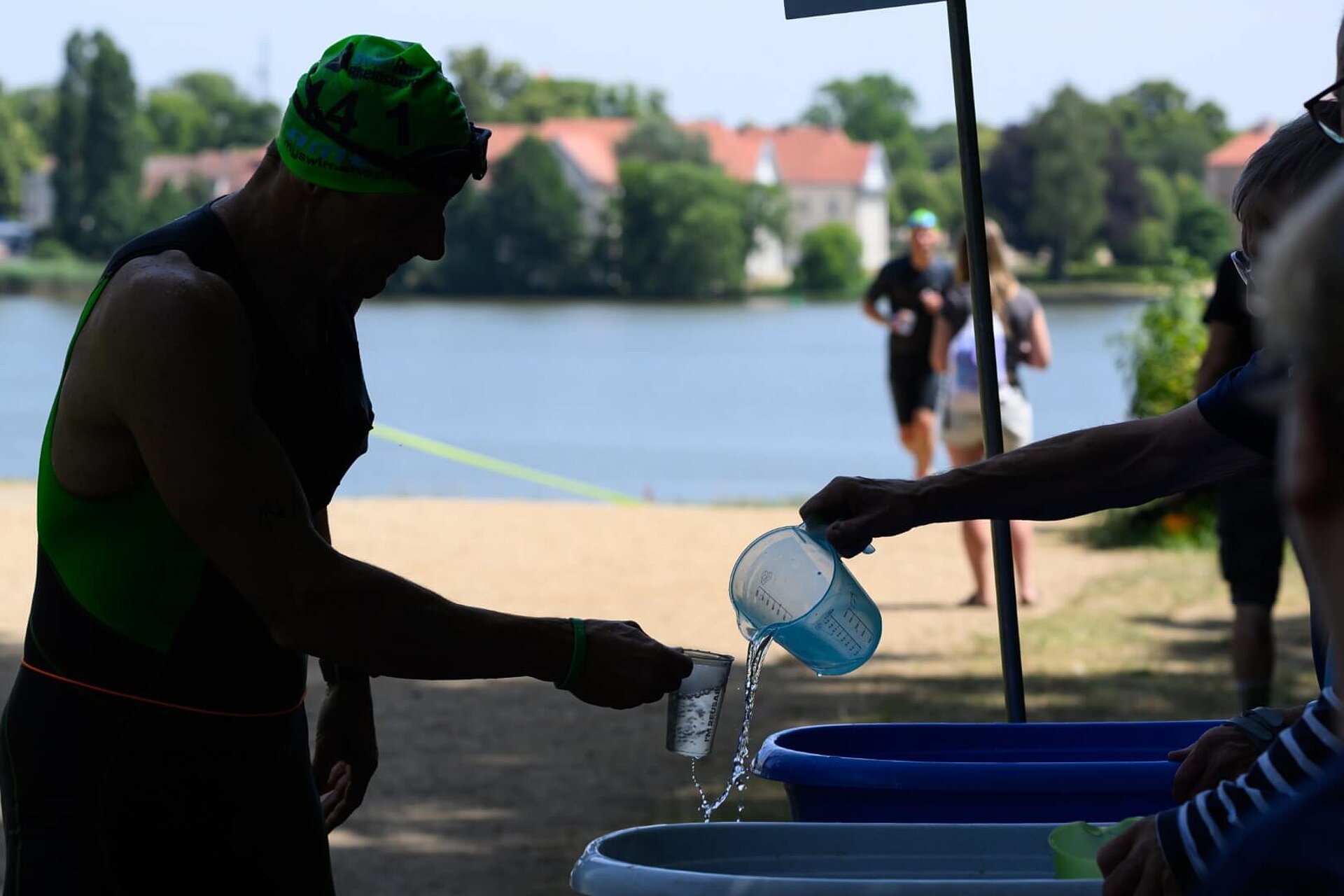 An einem schattigen Stand bekommt ein Teilnehmer seinen Becher mit Wasser aus Plastikwannen befüllt.