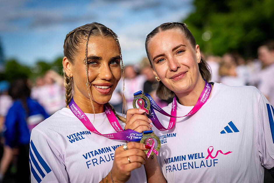 Two happy participants wearing Women's Race T-shirts hold up their medals for the camera.