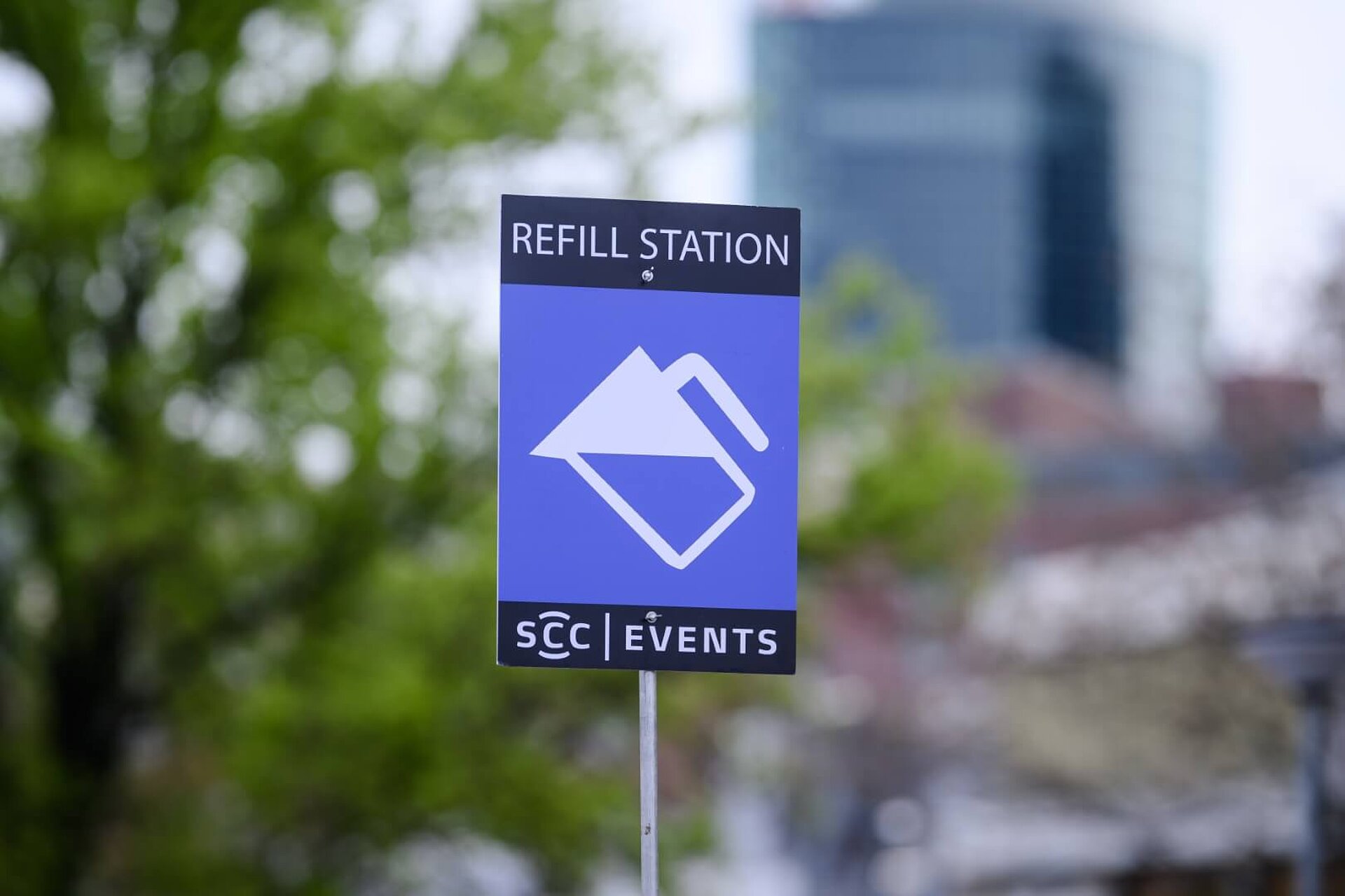 Blaues Schild von SCC EVENTS mit Beschriftung "Refill Station" und einer symbolischen Wasserkaraffe in weiß.