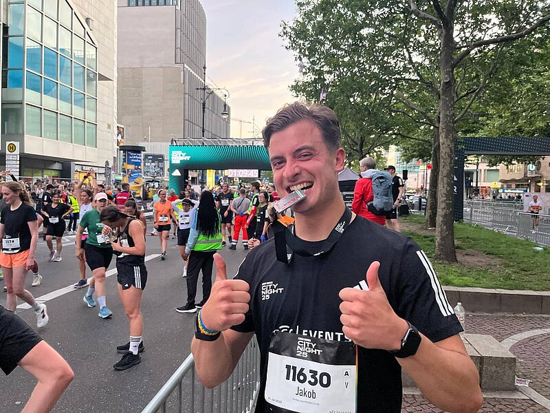 Jakob Wartchow cheerfully gives a thumbs up and bites his adidas Runners City Night medal.