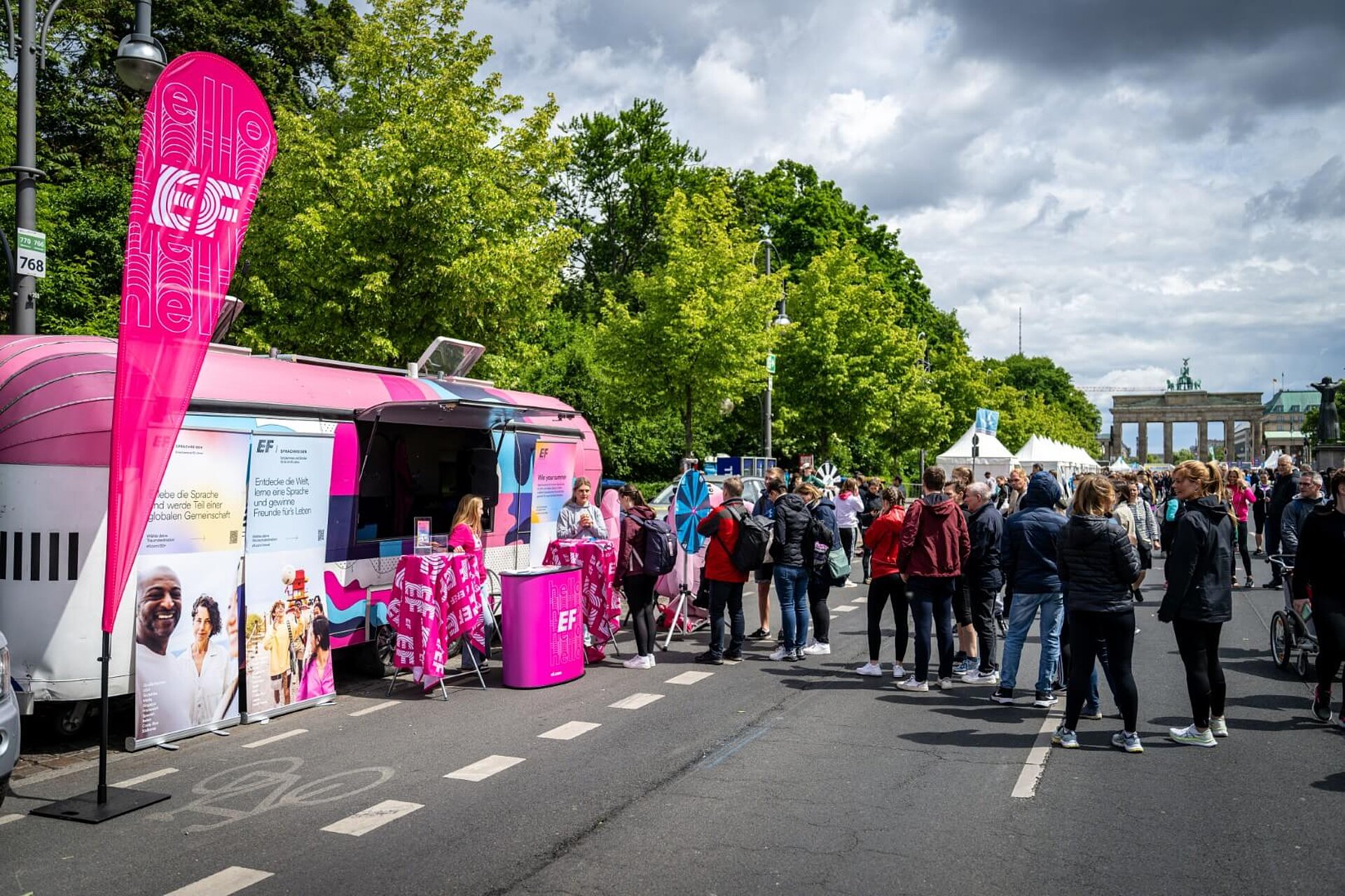 Kleine Menschentraube vor rosa-pinkem Trailer von EF. Brandenburger Tor im Hintergrund.