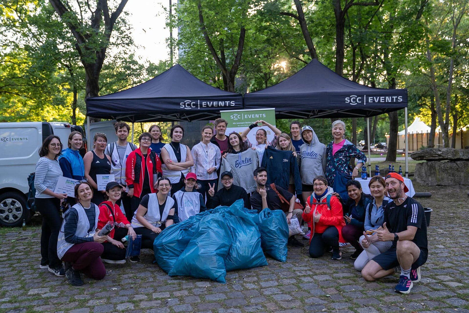 Etwa zwei Dutzend lächelnde Teilnehmende posieren hinter einem kleinen Haufen gefüllter Müllsäcke für ein Gruppenfoto.