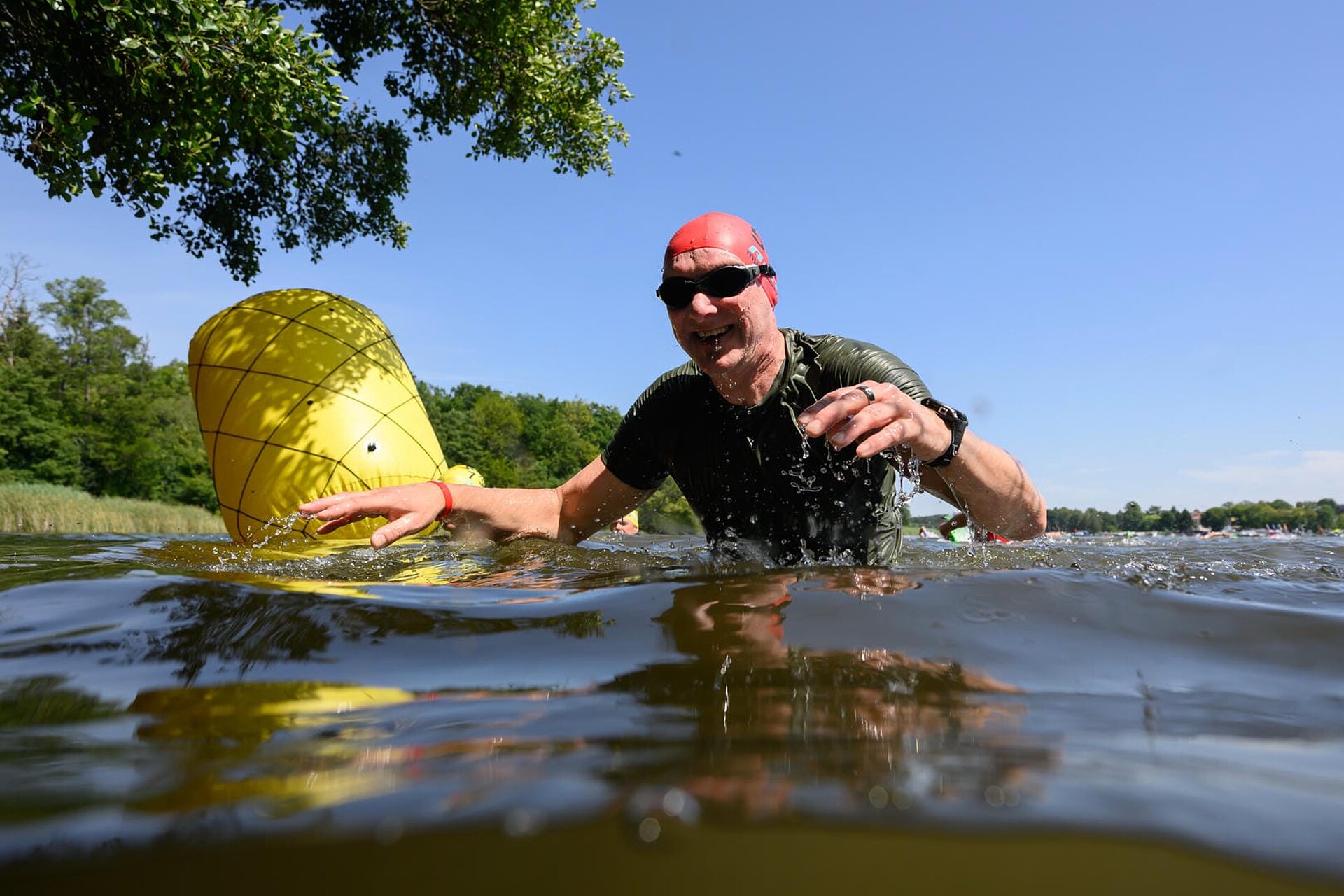 Lachender Teilnehmer mit Schwimmbrille stapft durch bauchtiefes Wasser Richtung Ufer.