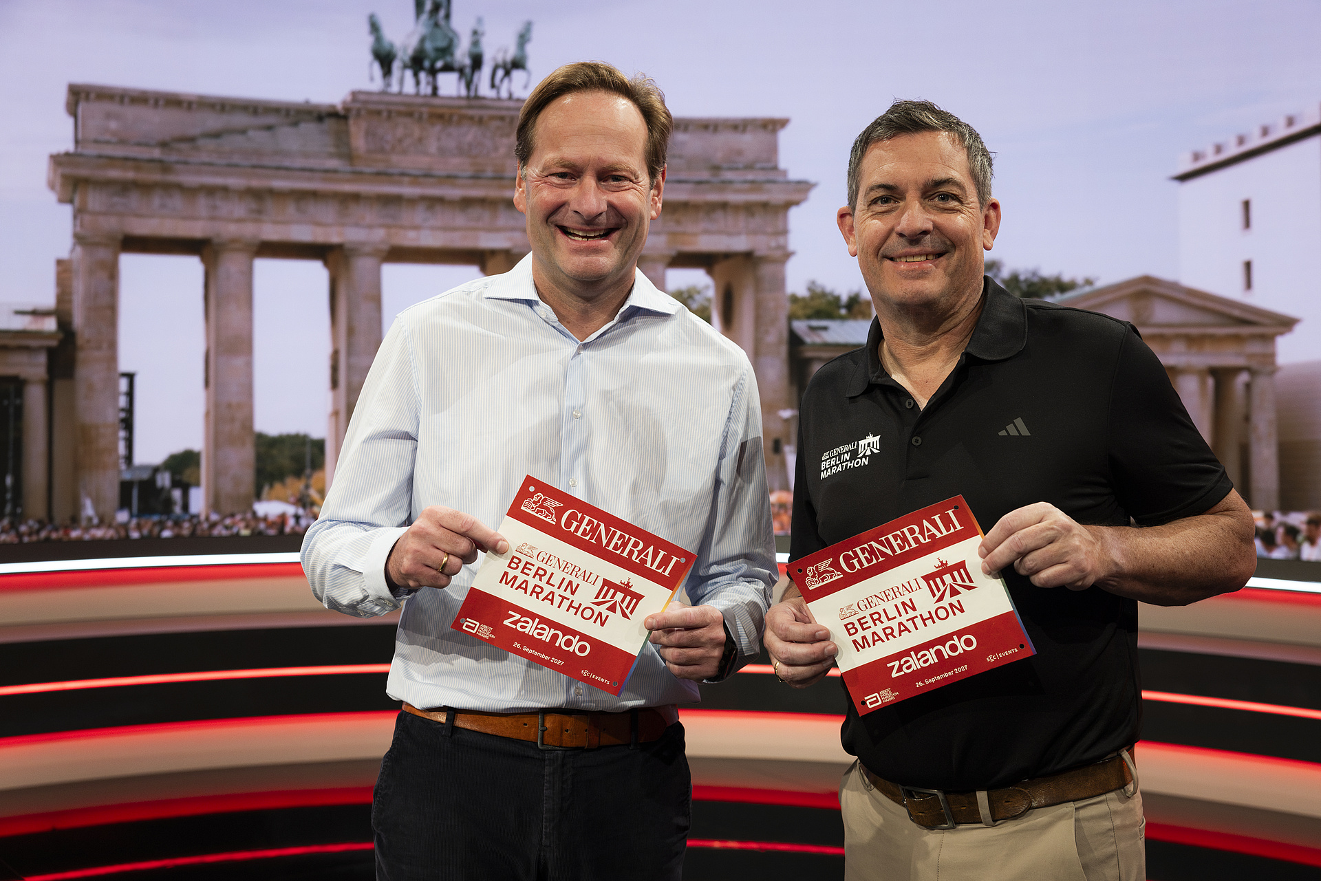 Die beiden CEOs halten lächelnd eine Startnummer mit dem Generali Berlin-Marathon Logo in die Kamera.