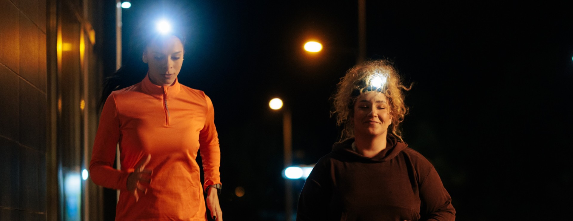 Zwei Frauen mit Stirnlampen joggen im Dunkeln.